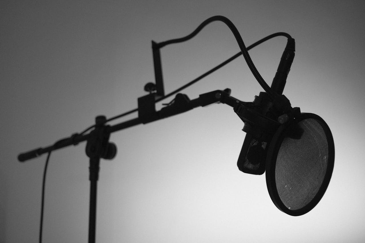 our-experience Black and white image of a professional studio microphone with a boom arm and pop filter.