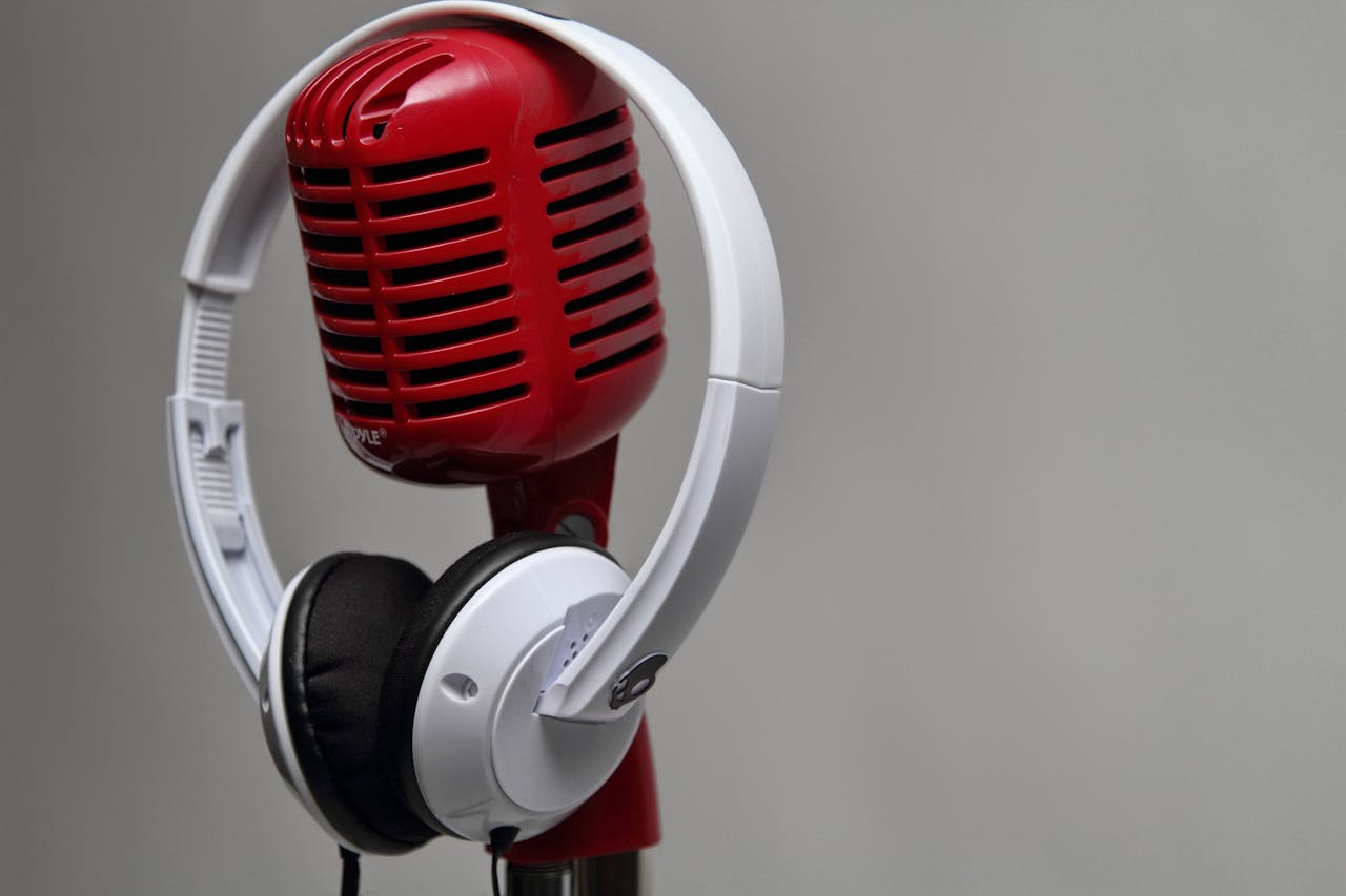 Close-up of a red vintage microphone with white headphones against a gray background.