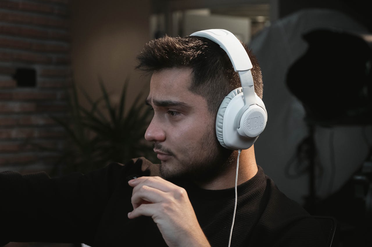 A man wearing headphones focused in a modern indoor studio setting, possibly a radio host or audio professional.
